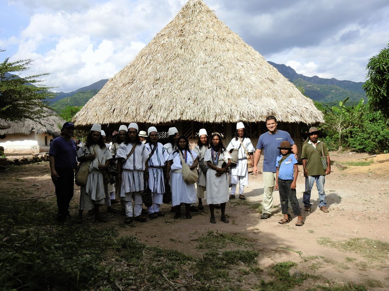 Group of people standing outside of a building with a thatched roof 